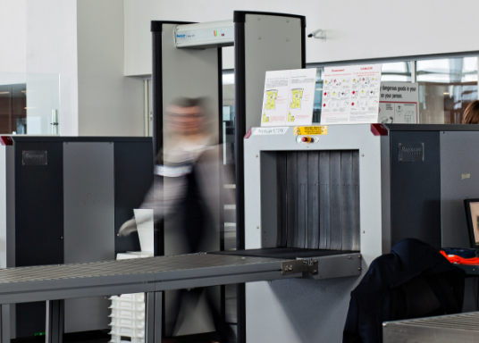 Individual passing through Metal Detector and X-Ray Screening in progress.